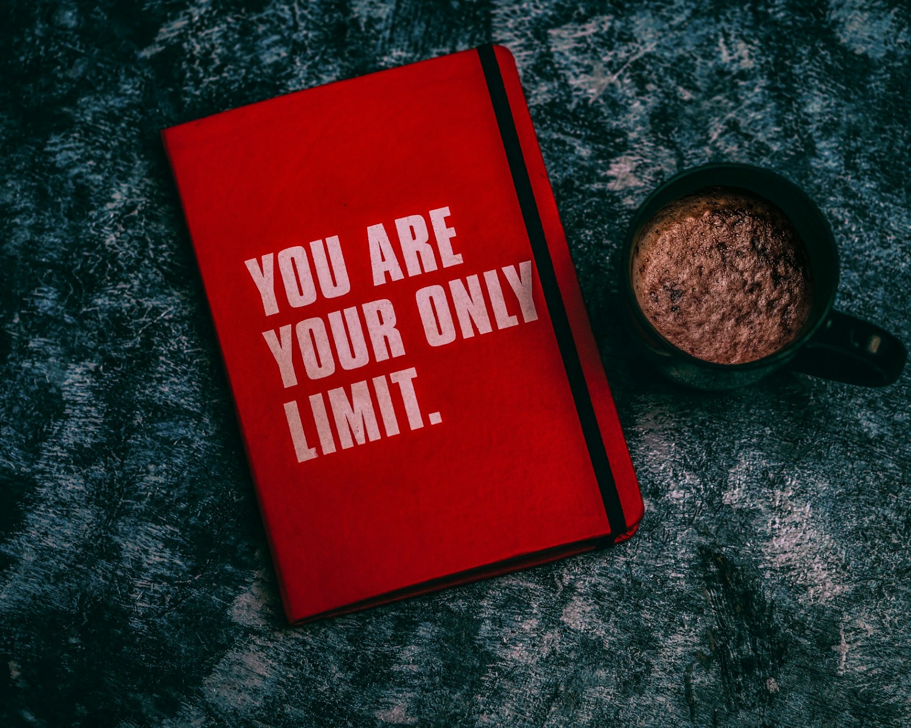 a red book with the words you are your only limit next to a cup of